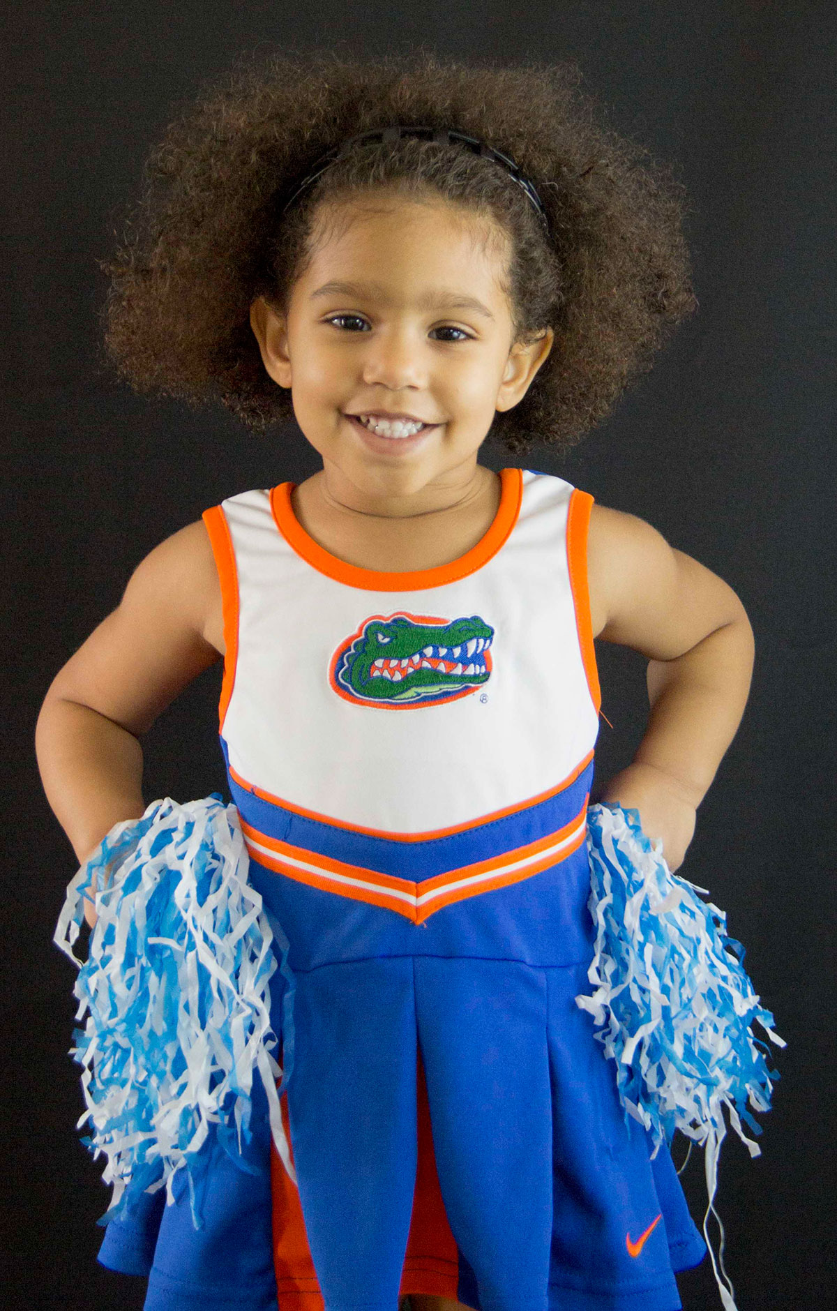 Young cheerleader portrait in blue and orange uniform holding pom-poms